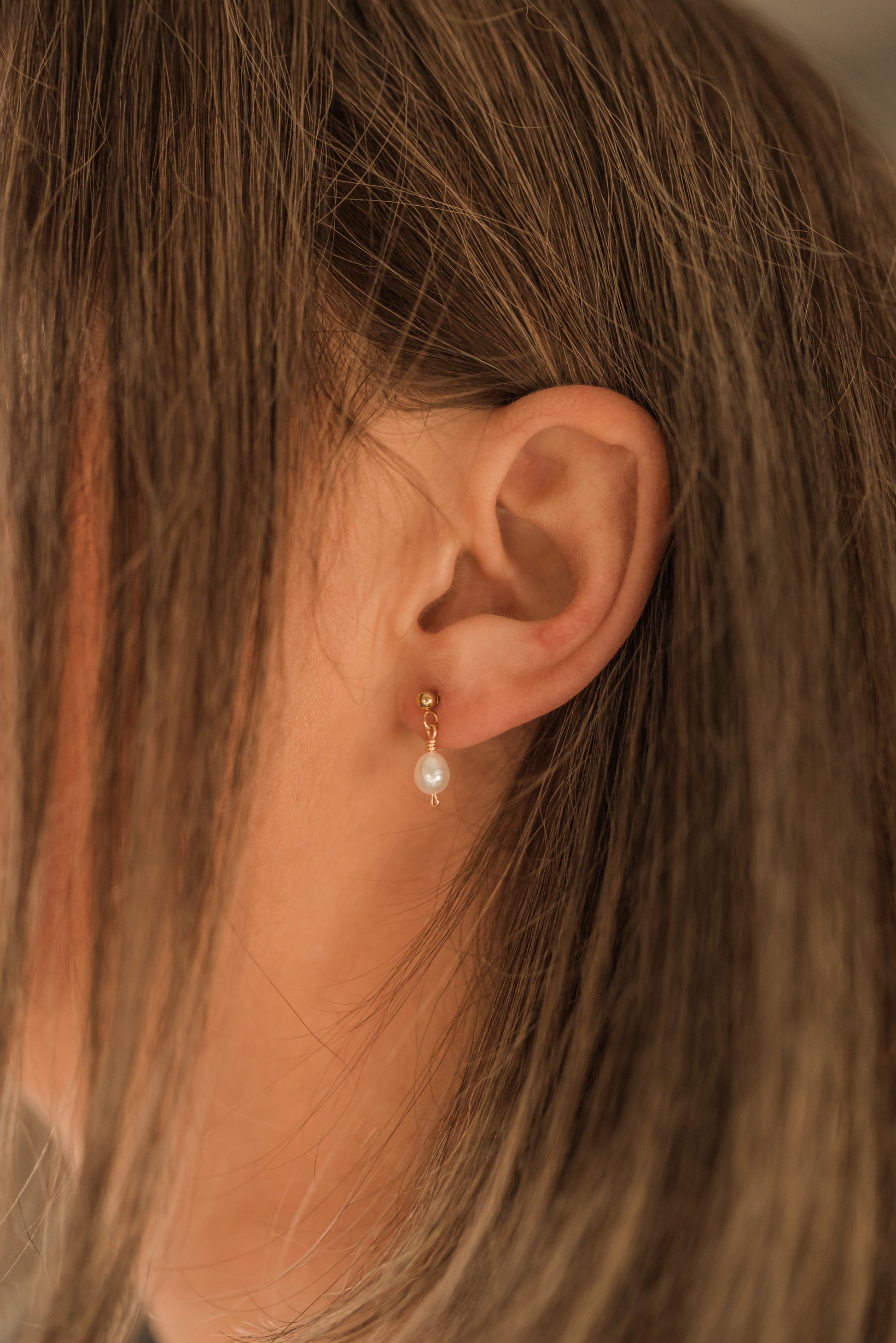 Detail minimalistické perlové náušnice v uchu modelky pro každodenní nošení.