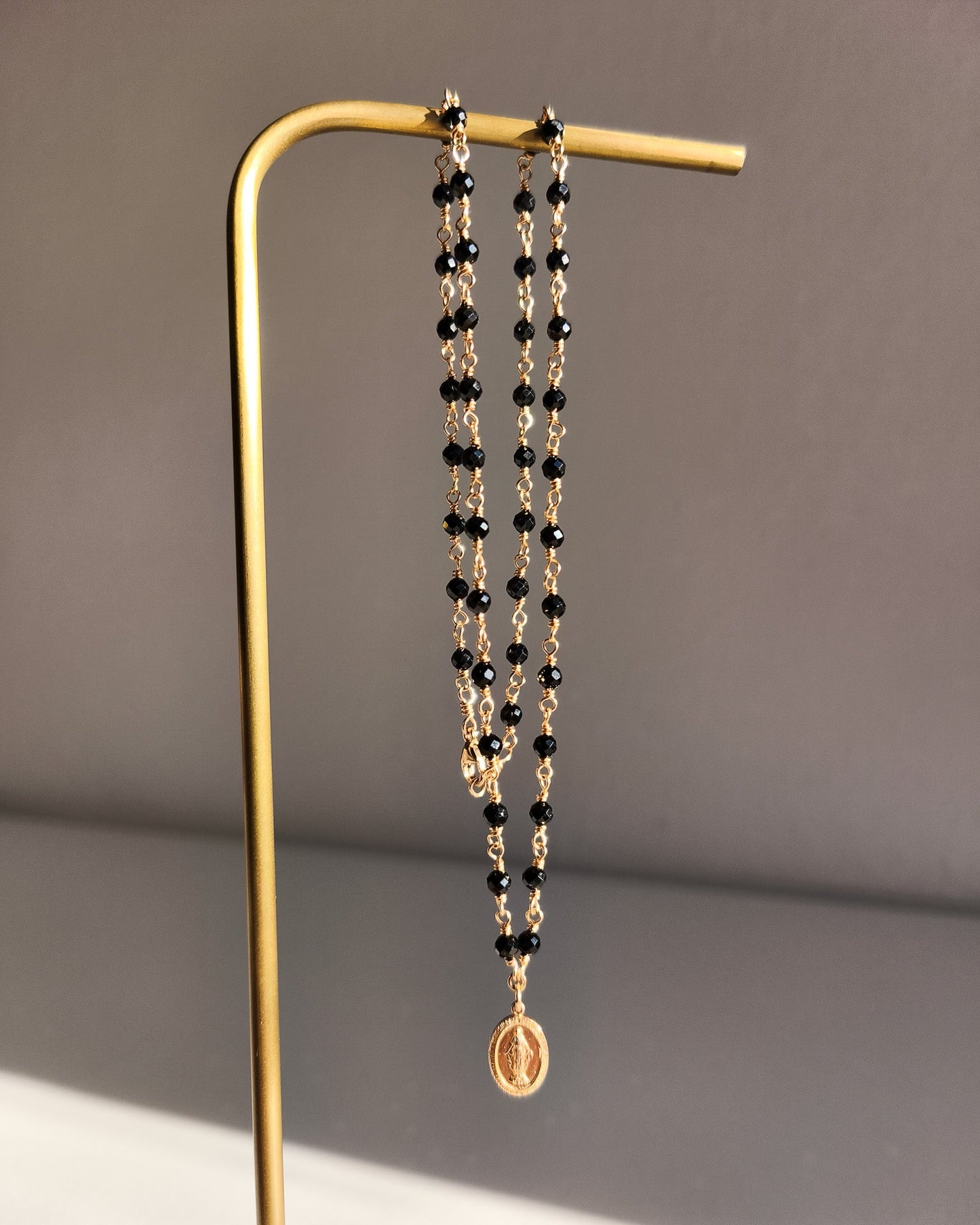 Náhrdelník z třpytivého 14k gold filled a černého spinelu s přívěskem madonky.