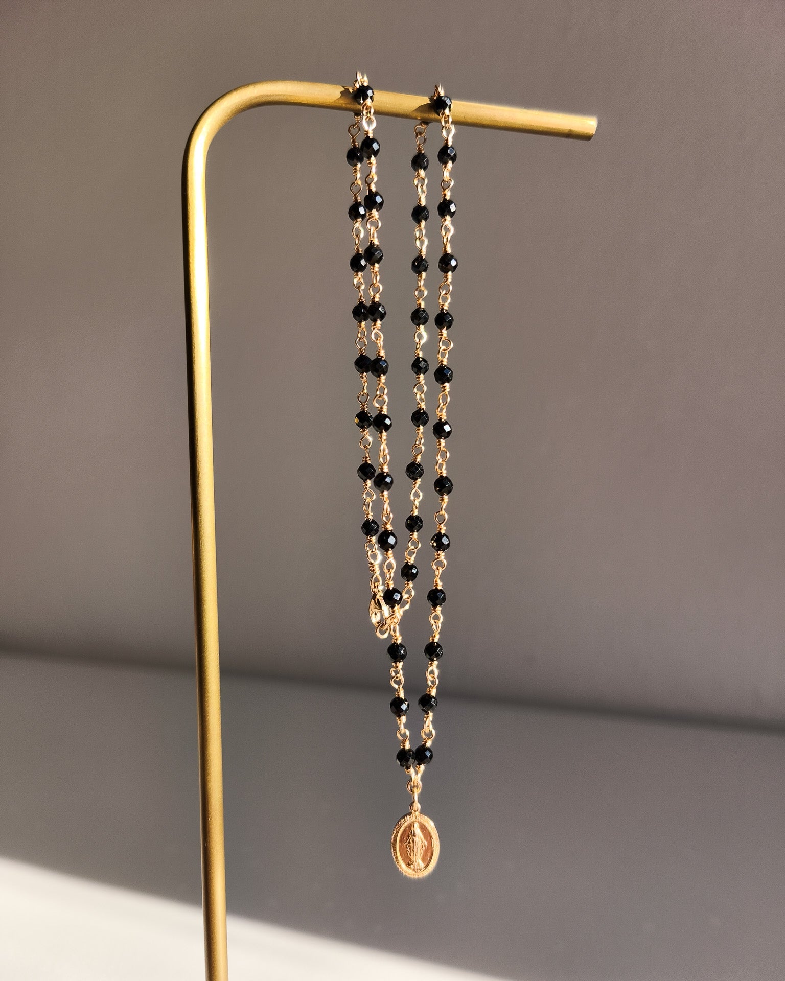 Náhrdelník z třpytivého 14k gold filled a černého spinelu s přívěskem madonky.
