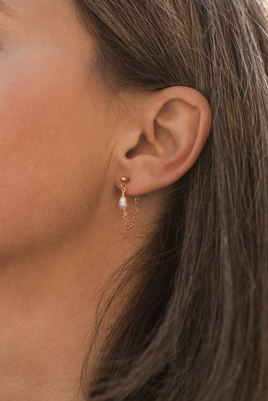 Detail řetízkových perlových náušnic v uchu modelky pro elegantní a minimalistický vzhled.