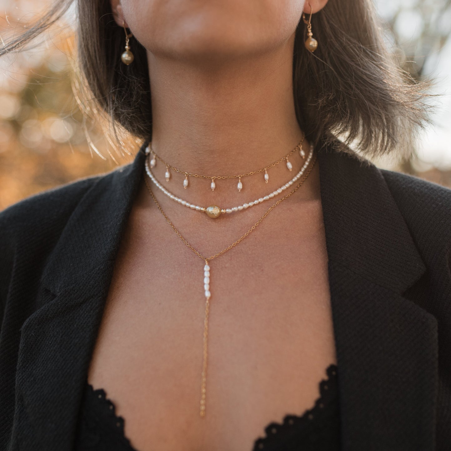 Inspirace pro vrstvení náhrdelníků: krátký zlatý choker s perličkami v kombinaci s dalšími náhrdelníky.