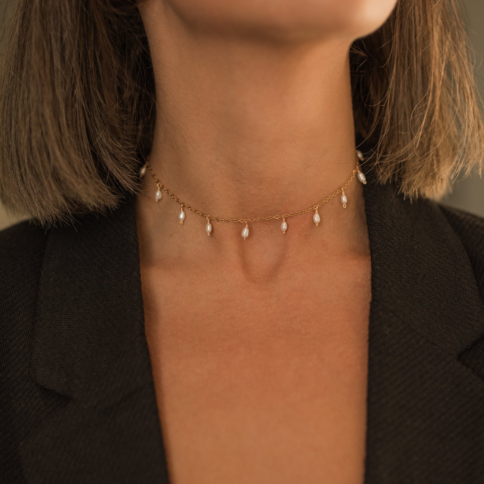 Detailní pohled na lesklý řetízkoý choker  náhrdelník s perličkovými přívěskyna krku modelky.