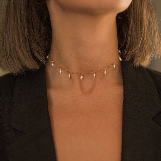 Detailní pohled na lesklý řetízkoý choker  náhrdelník s perličkovými přívěskyna krku modelky.